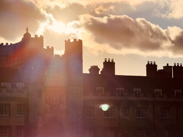 Sunset light flares behind silhouetted rooftops and chimneys beneath layered clouds
