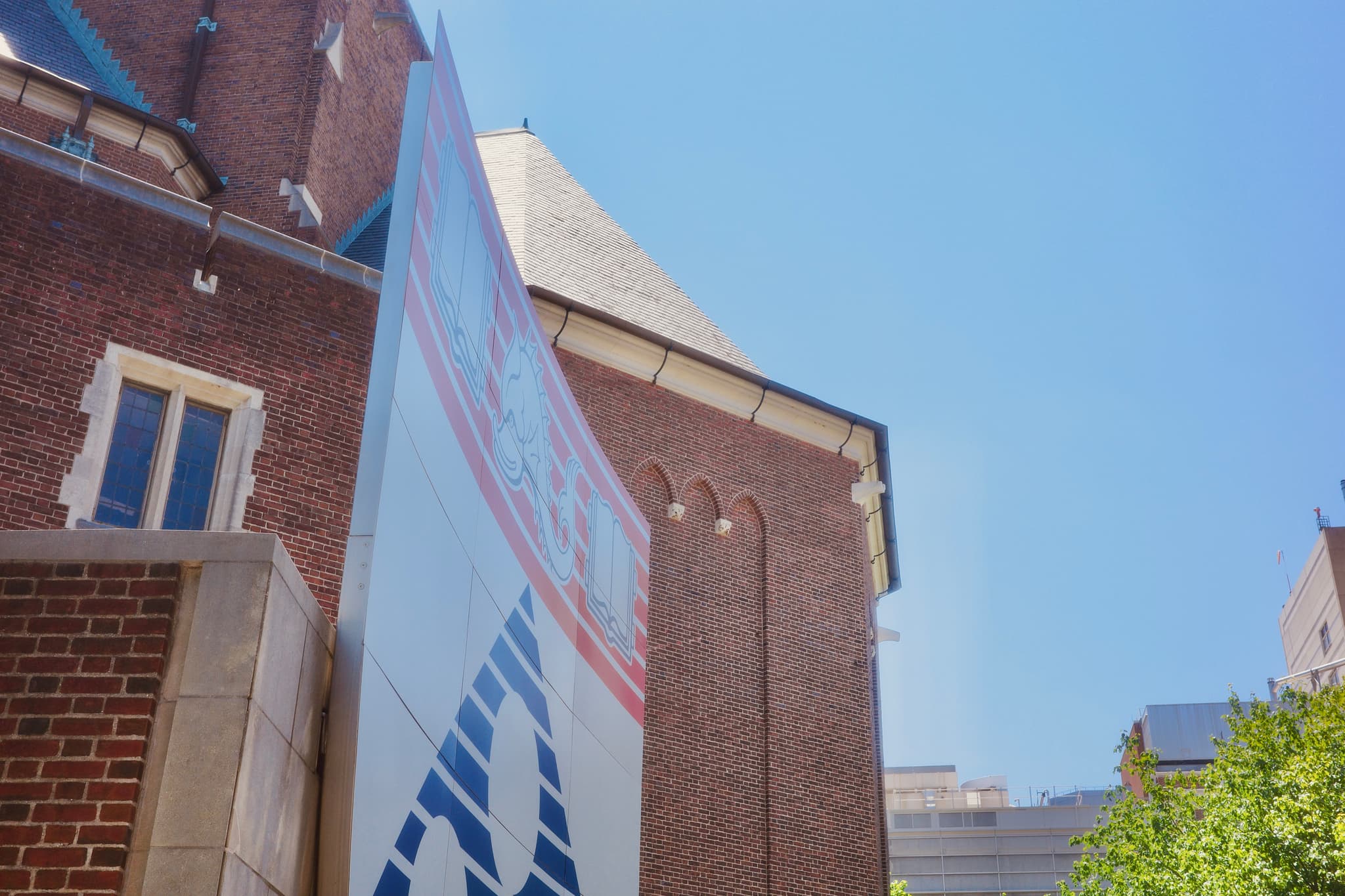 Low-angle view of a tall banner mounted between brick campus buildings under a blue sky