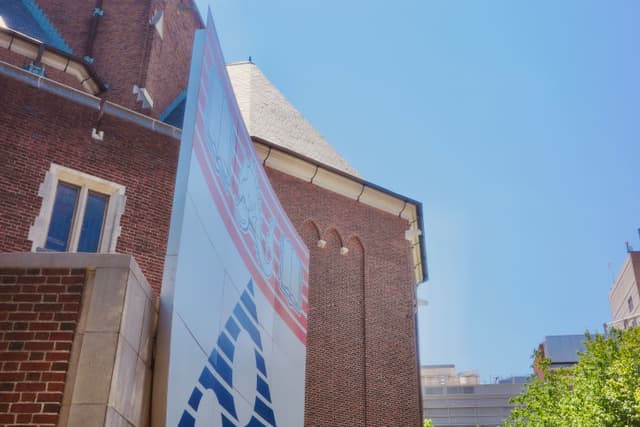 Low-angle view of a tall banner mounted between brick campus buildings under a blue sky
