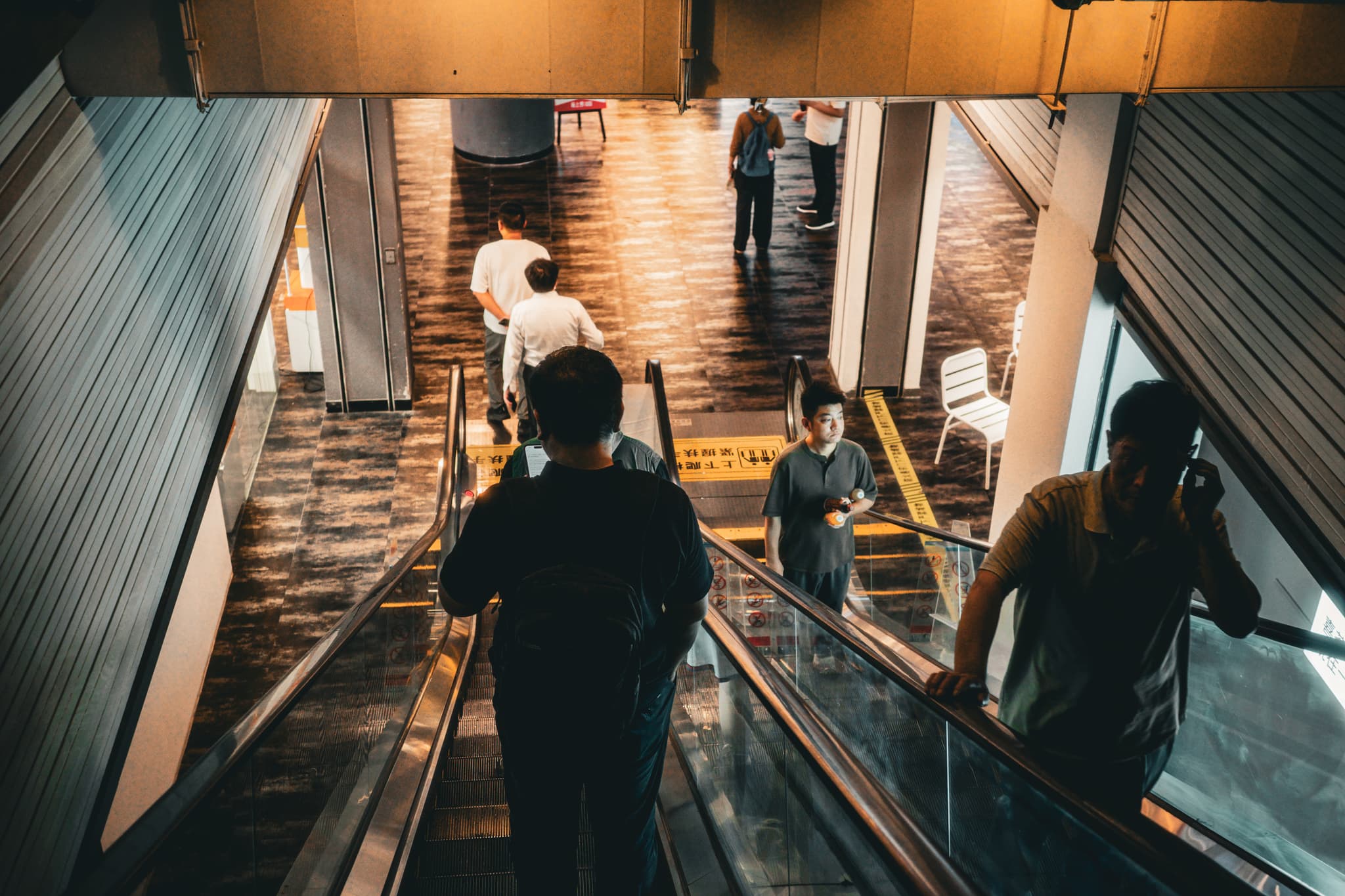 People using escalators in a dimly lit indoor space with a reflective floor and modern architecture