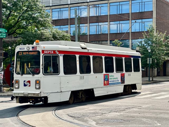 A white SEPTA trolley with red and blue accents traveling on a street near a modern building