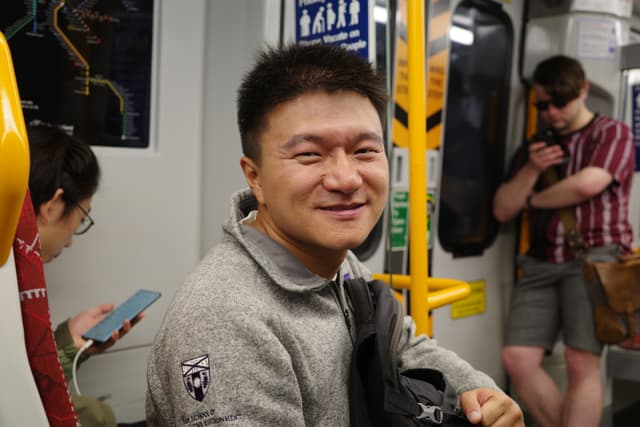 Smiling passenger seated inside a subway car while other riders stand nearby