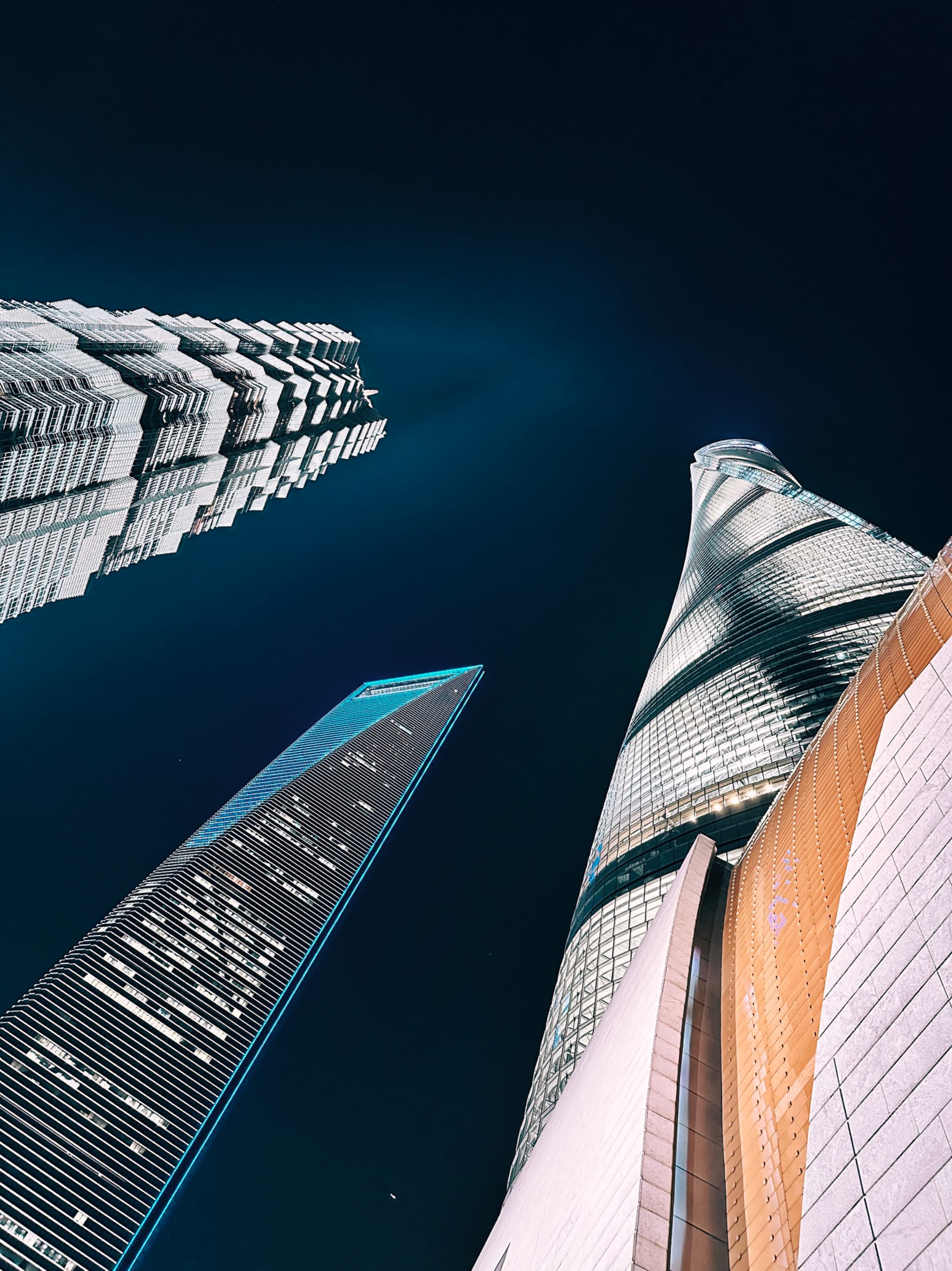 A night sky serves as the backdrop for a dramatic upward view of several towering skyscrapers, showcasing their modern architecture and illuminated windows