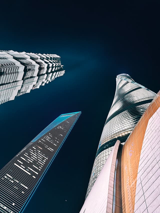 A night sky serves as the backdrop for a dramatic upward view of several towering skyscrapers, showcasing their modern architecture and illuminated windows