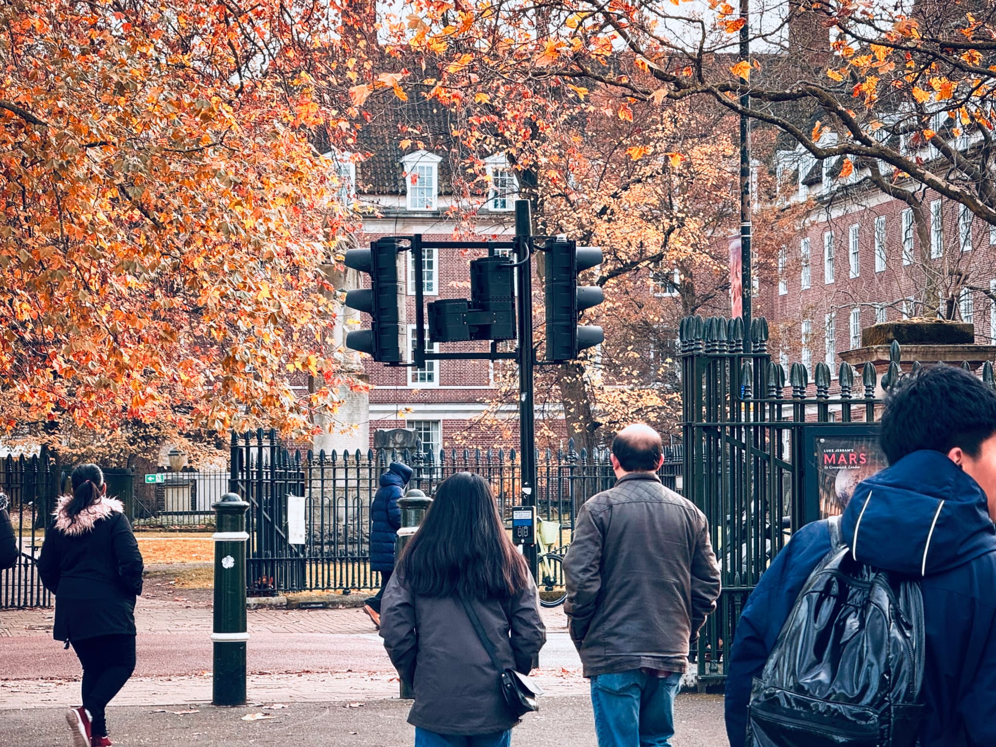 People walking near a gated area surrounded by autumn trees and urban architecture