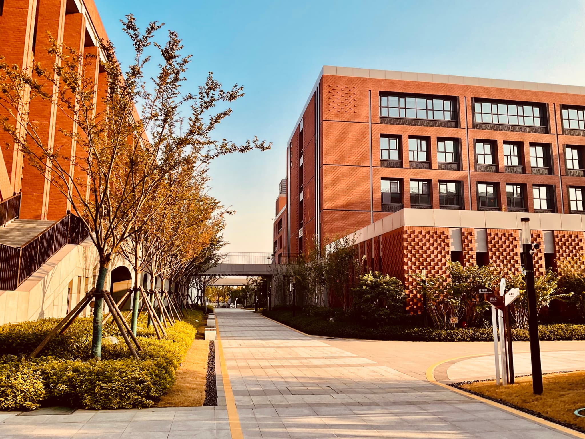 A campus walkway flanked by red-brick buildings and trees under a clear sky