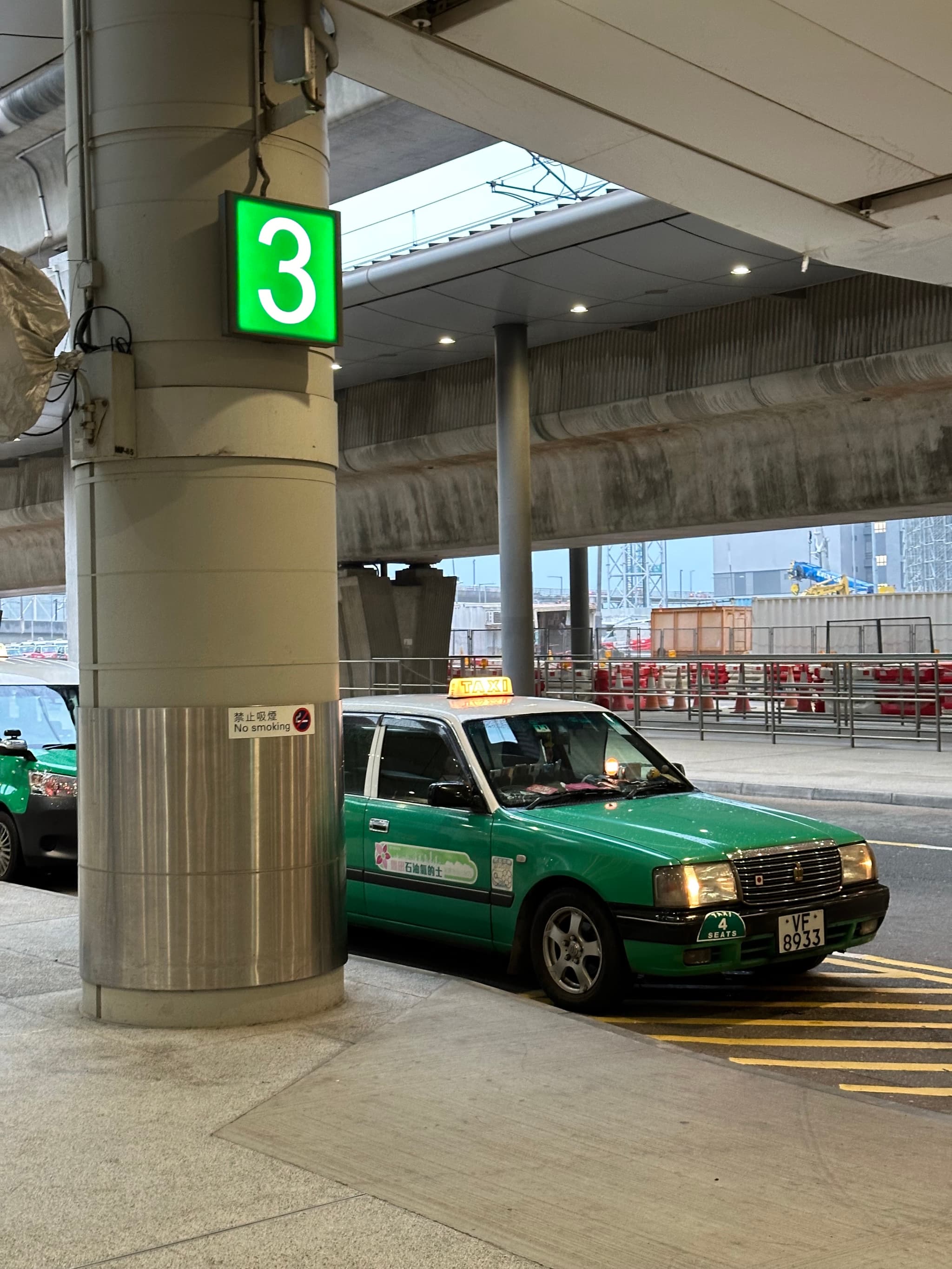 A green taxi parked beside a column with a green pharmacy cross sign, in an indoor setting with a high ceiling and visible infrastructure The photo is rotated 90 degrees to the left