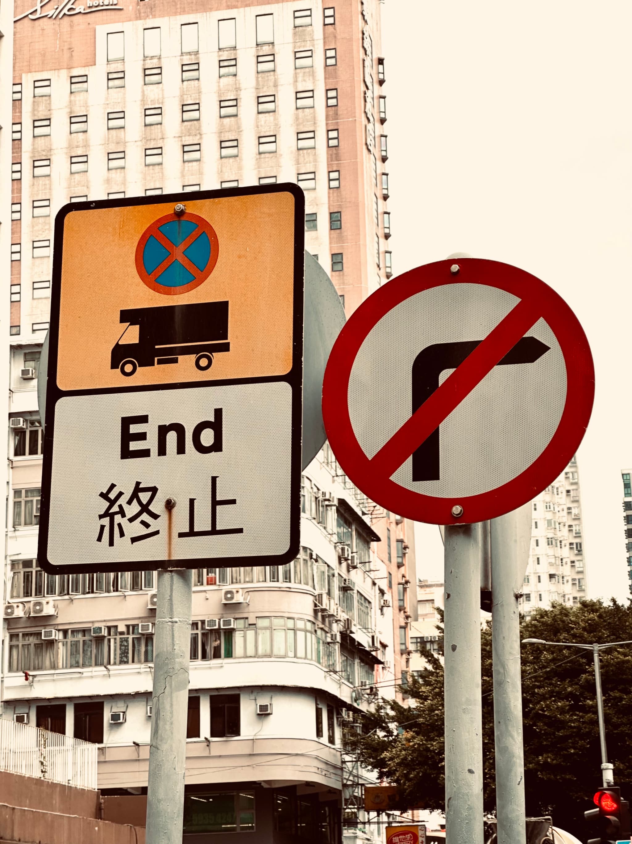 A traffic signpost featuring a no parking sign and another indicating the end of a restriction, with Chinese characters below the English word End, set against an urban backdrop with a high-rise building