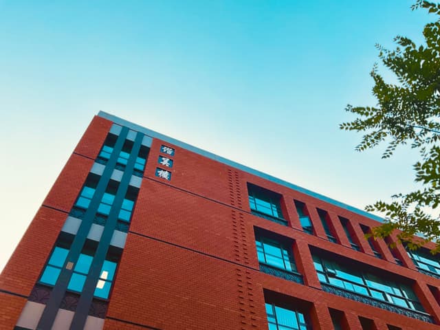 A low-angle view of a red brick school building against a clear blue sky