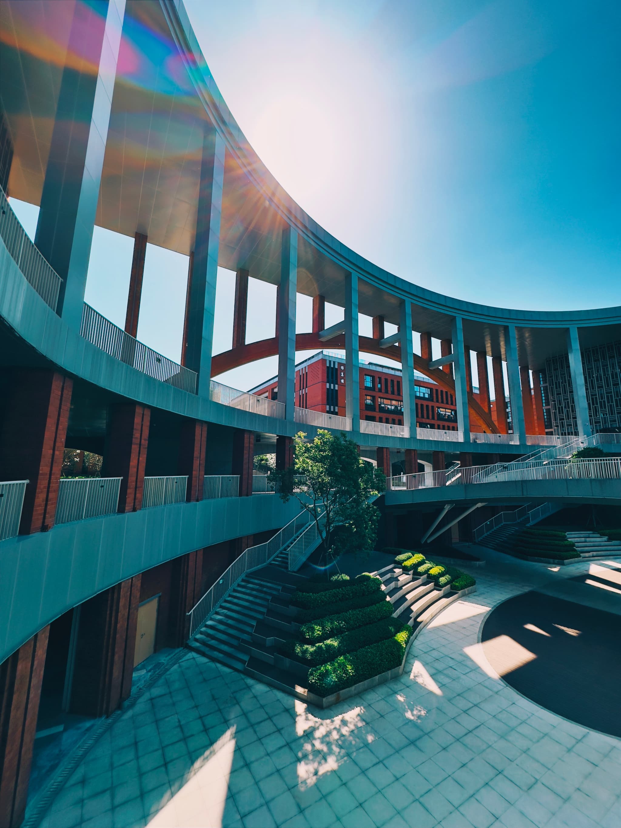 A modern architectural structure with curved lines, vibrant red accents, and a sunburst effect in a clear blue sky