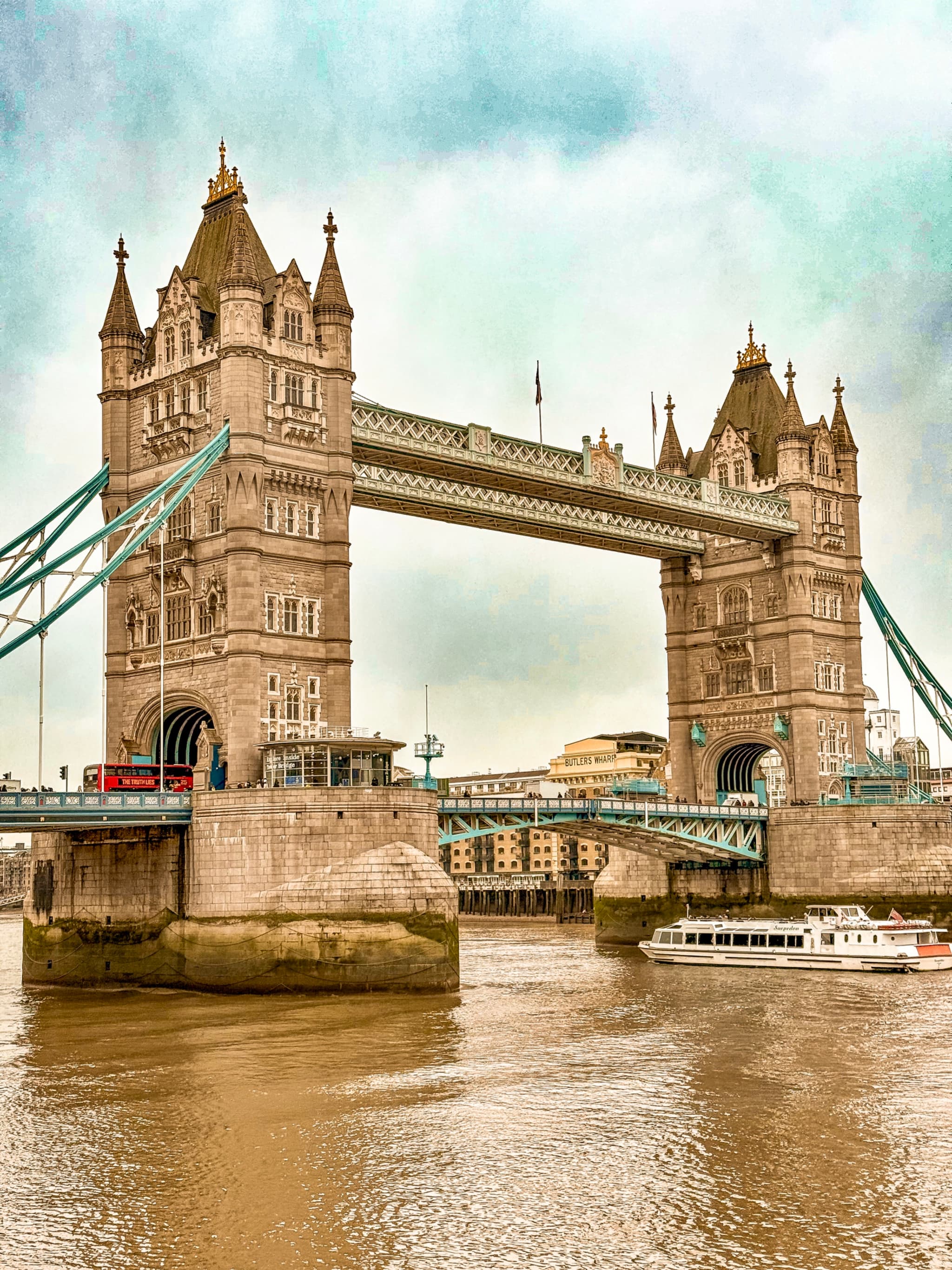 Tower Bridge spanning the River Thames, with a red double-decker bus crossing and a boat passing below