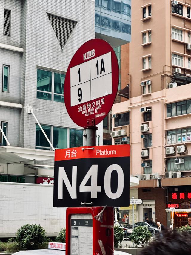 A bus stop sign with the number N40 and a list of bus routes 1, 1A, and 9, set against an urban backdrop with buildings and a glimpse of a storefront