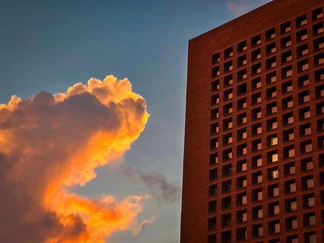 A high-rise building with a patterned facade against a backdrop of a sunset sky with orange-tinged clouds