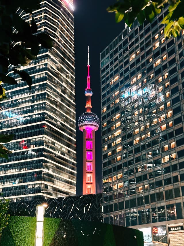 A nighttime cityscape featuring the illuminated Oriental Pearl Tower amid surrounding skyscrapers