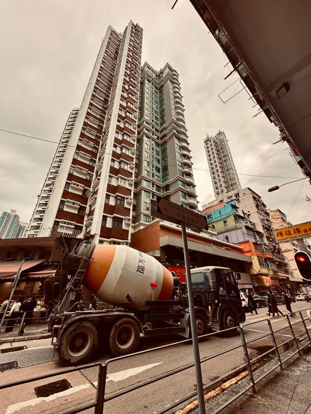 A cement mixer truck on a city street with tall residential buildings in the background under an overcast sky