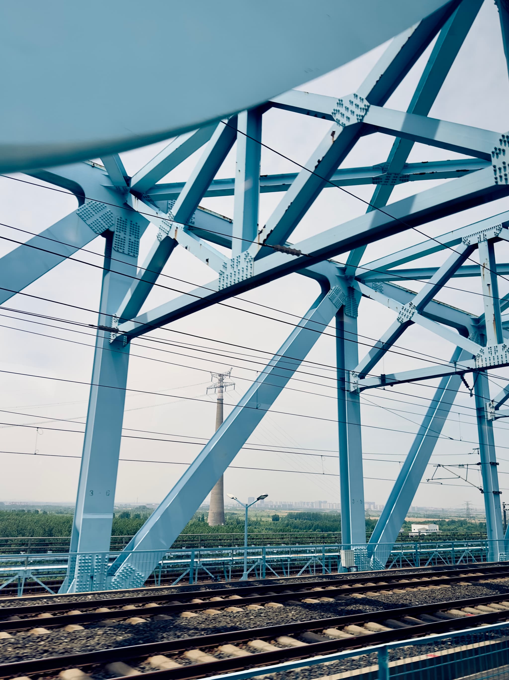 A blue steel truss structure, part of a bridge, with railway tracks in the foreground and power lines in the background